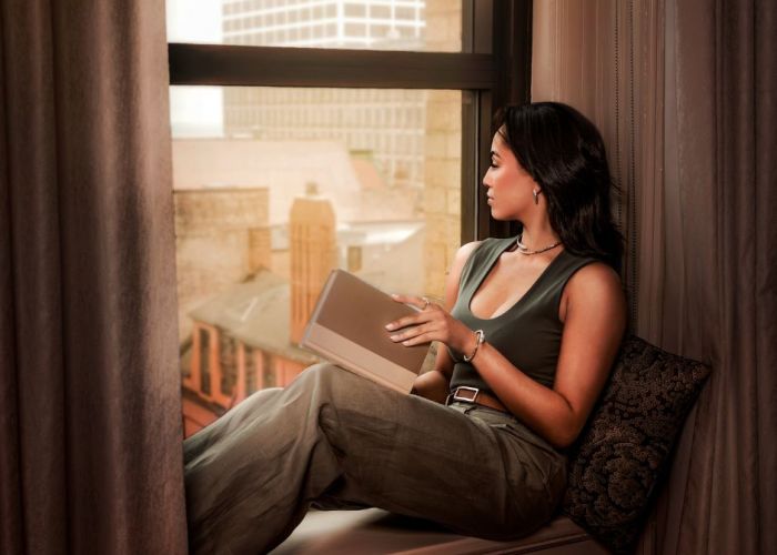 A woman sits in a window, reading a book but mostly contemplating the city outside the window