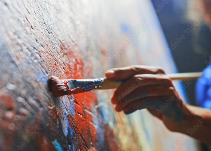 An image of a painter at a canvas, using a brush in oil paints.